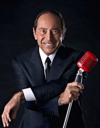 Une photo de Paul Anka en costume noir tenant un micro rétro rouge